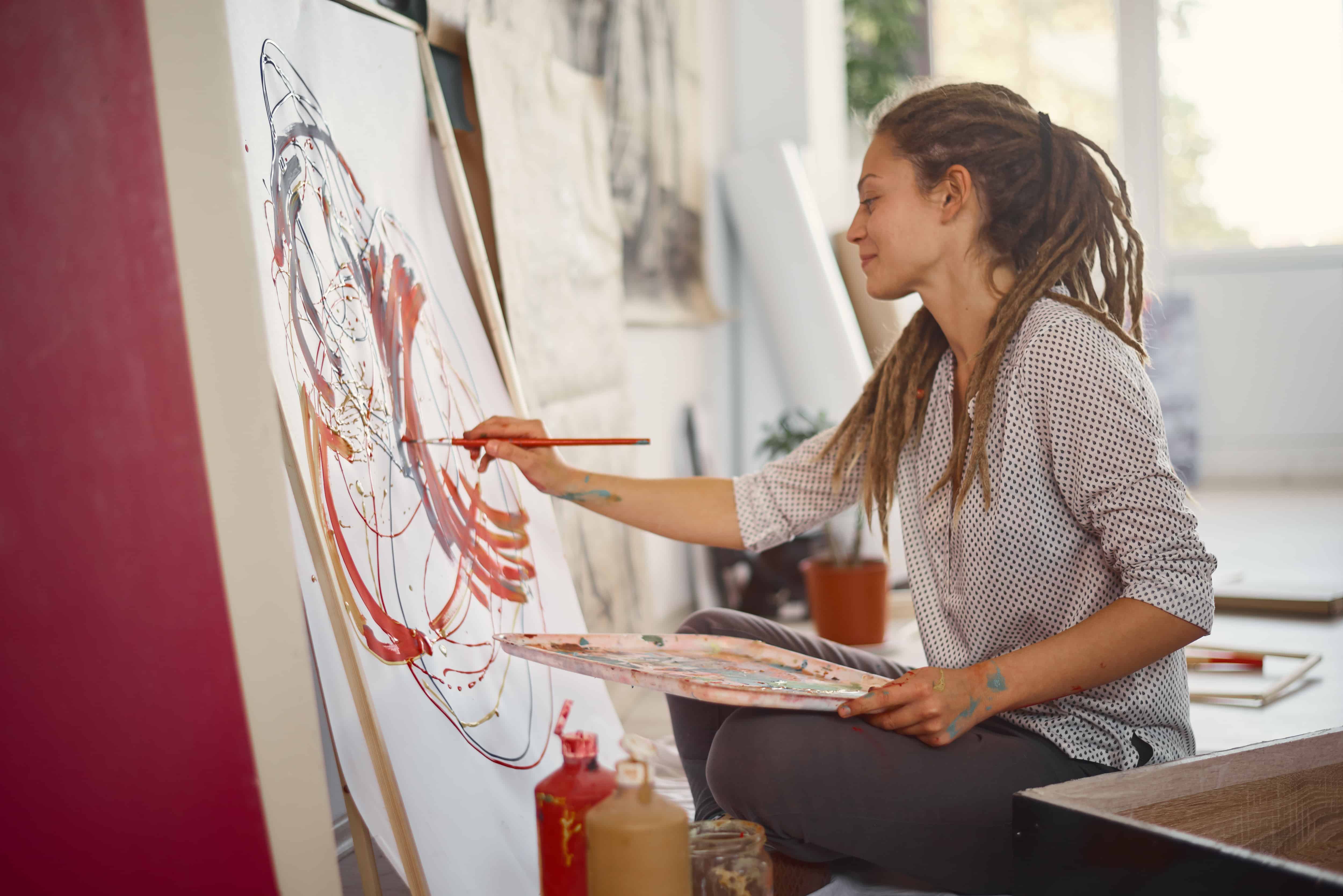 Artistic girl sitting in studio and paint on easel.