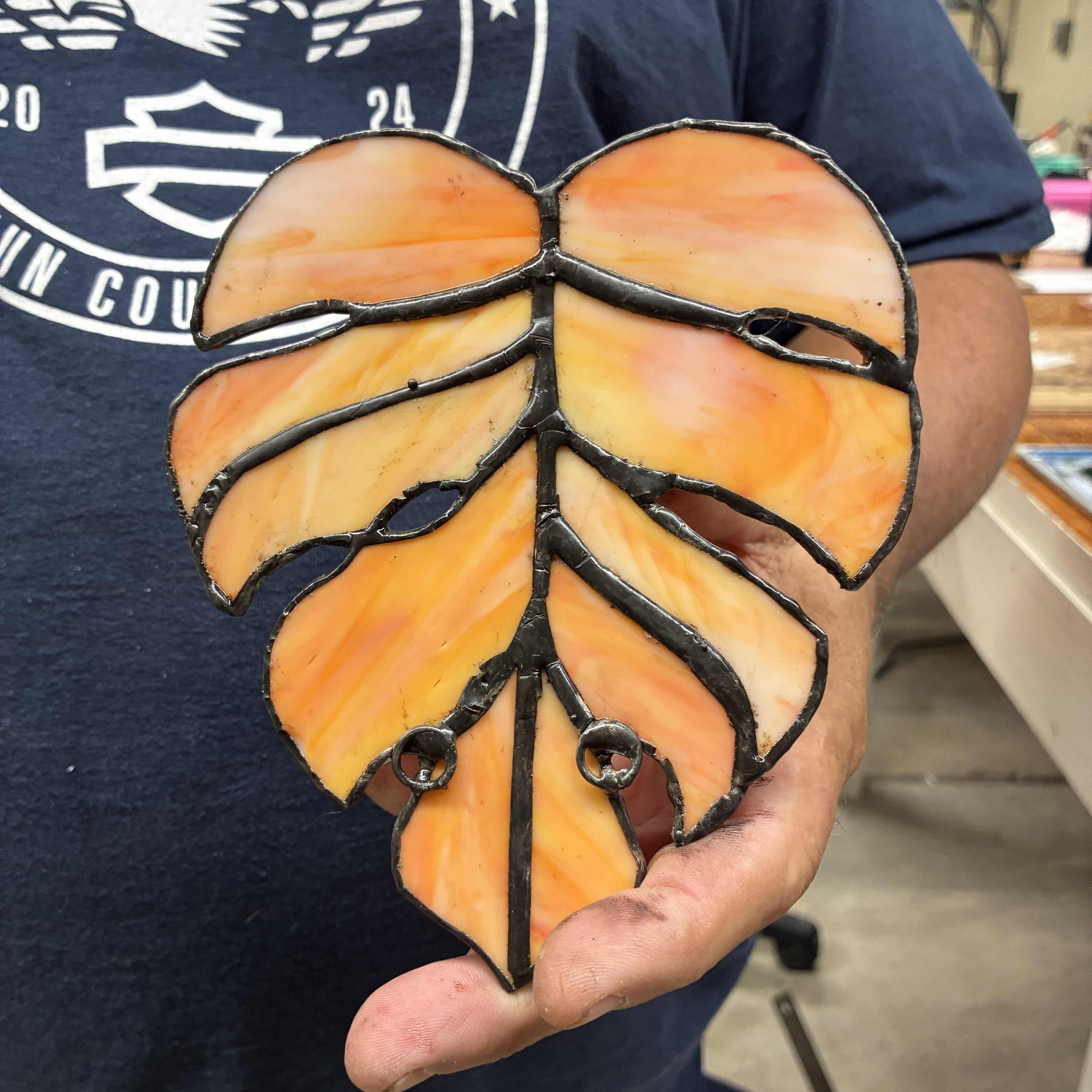 Student in a McNeese Leisure Learning stained glass class holding a completed stained glass leaf design.
