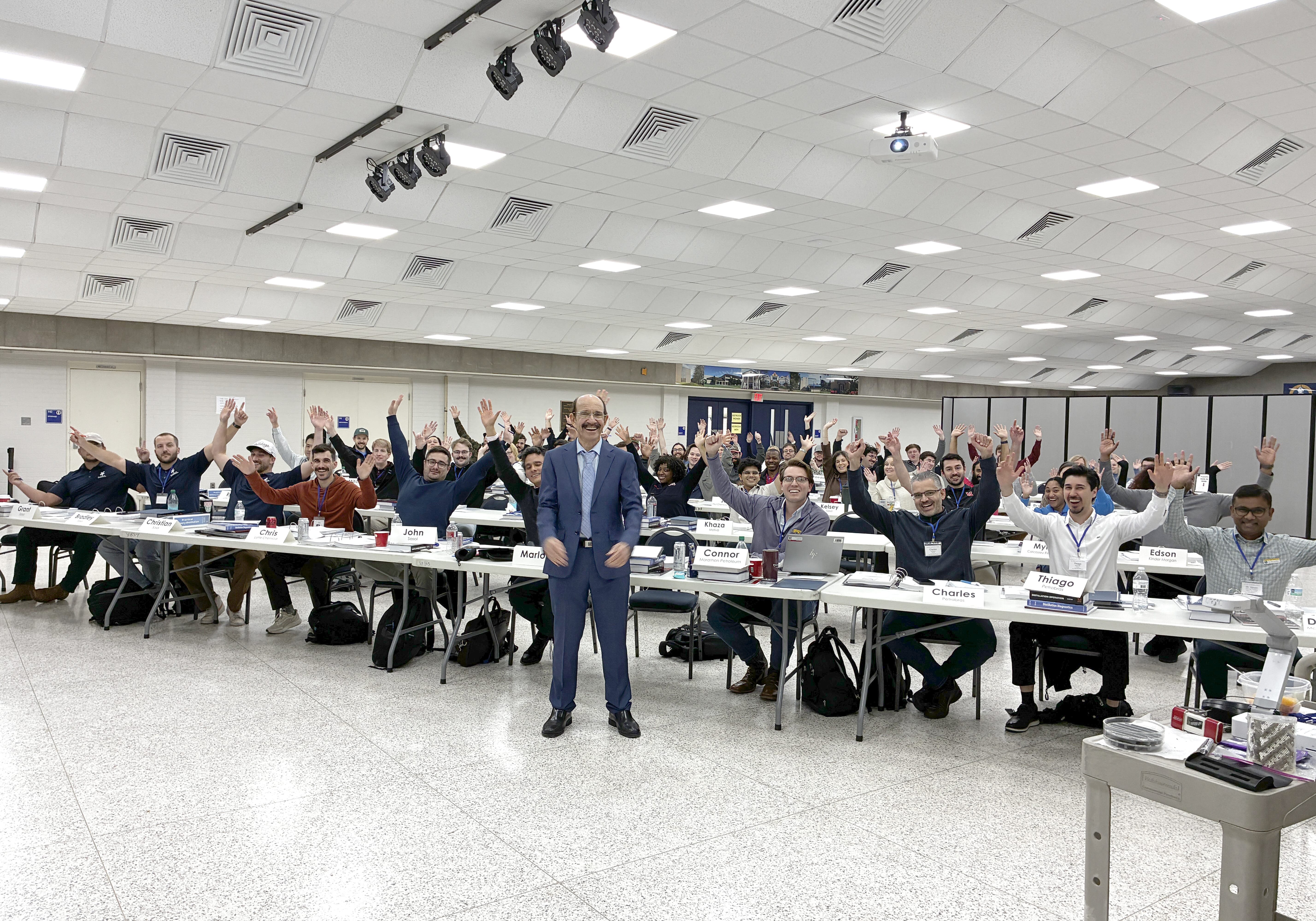 Henry Kister stands at the front of a distillation technology seminar while participants seated in a classroom raise their hands.