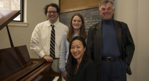 Dr. Lina Morita, Layton Bergstedt, Julianne Marler, and Bill Sherman gather around a piano.