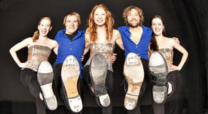 Members of The Step Crew stand with one leg up showing the bottom of their shoes.