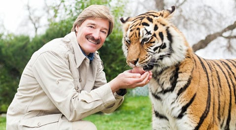 Peter Gros smiles at the camera while feeding a tiger.