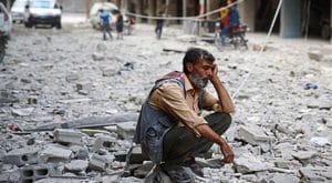 A man sits in the rubble of hard times in Syria