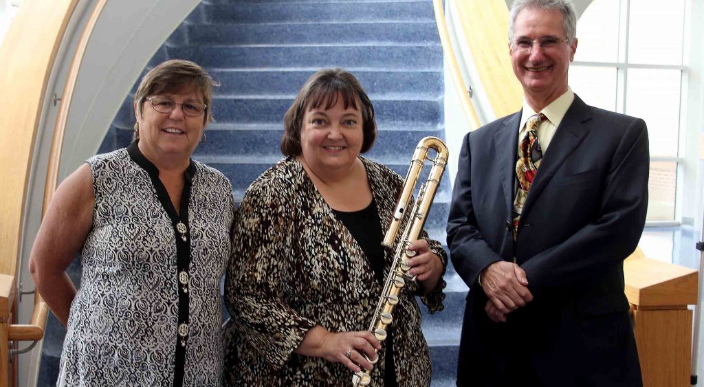 Catherine Robbins, Dr. Judy Hand, and David Robbins stand with the bass flute.