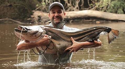 Zeb Hogan stands in water holding a large fish