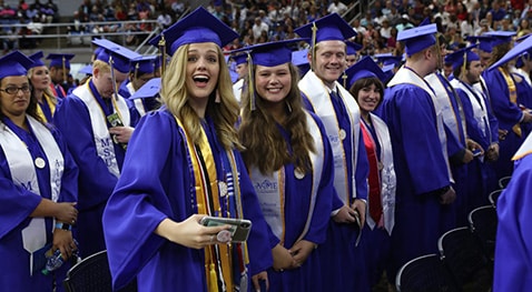 Undergraduate students in blue gowns smile for the camera as they anticipate the start of graduation.