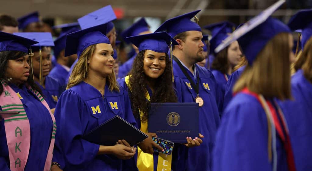 Graduates stand with their diploma covers as commencement ceremonies proceed.