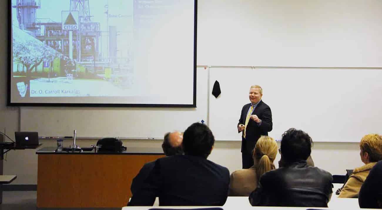 Dr. Mathis stands in the front of the classroom while using the screen to present slides on the BCST.