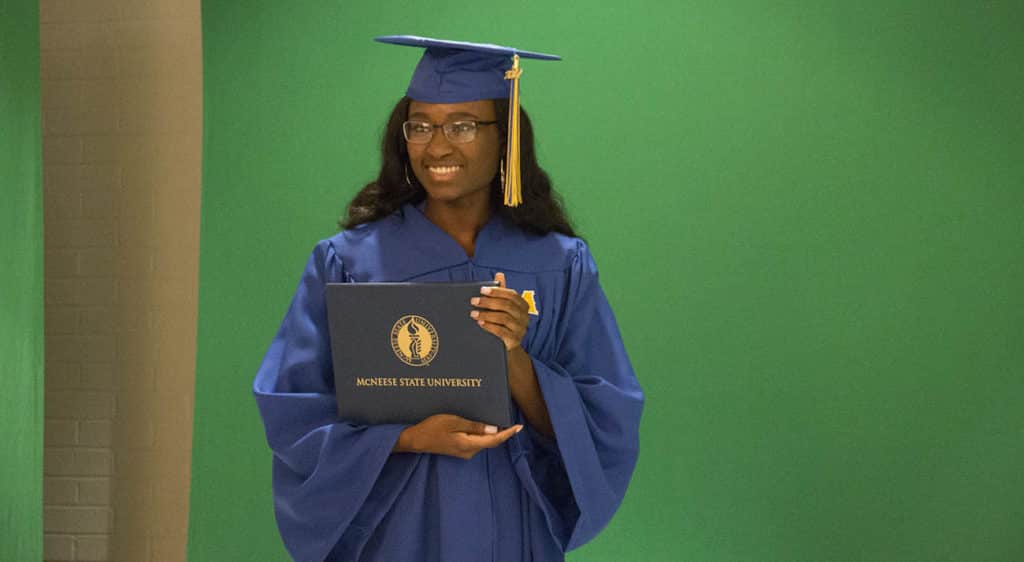 A female student stands with a diploma cover while getting her photo taken at GradFest.