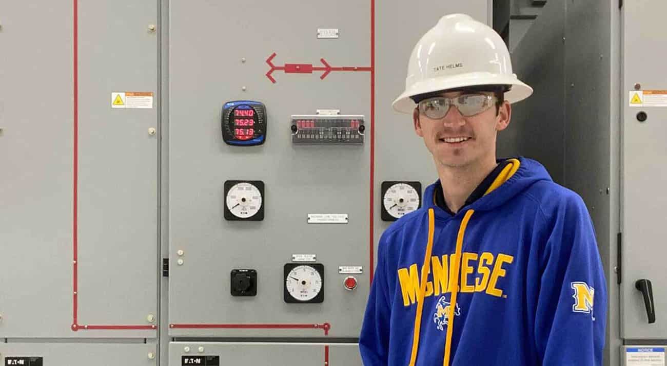 Tate Helms stands in front of machinery in a McNeese sweatshirt