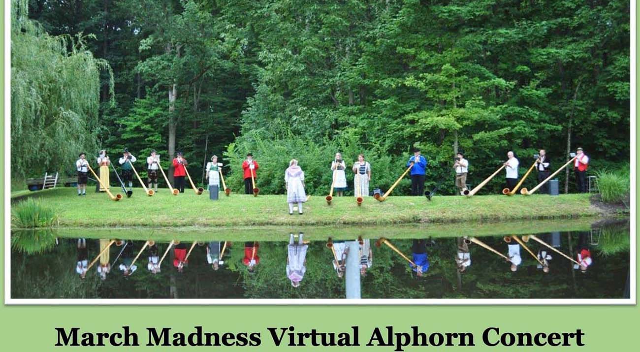 A group of Alphorn musicians stand in front of a body of water with their instruments.