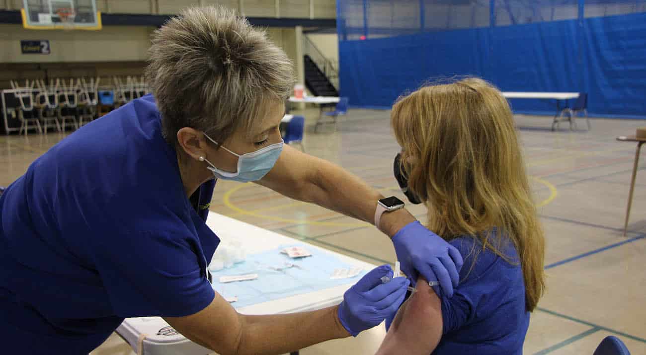 A nurse gives a young woman a covid vaccine in the arm.