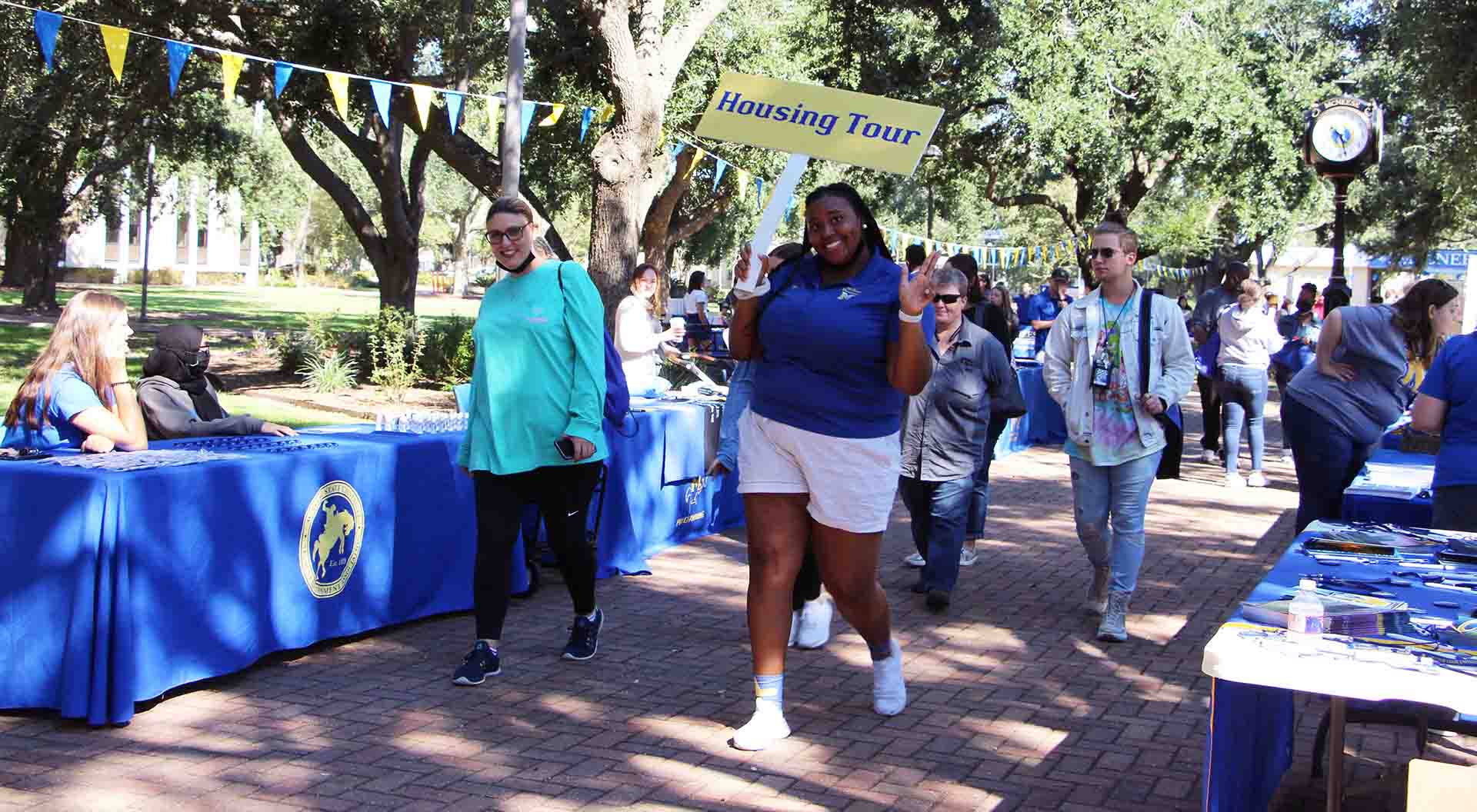 A student leads a group across campus with a sign that reads Housing Tour