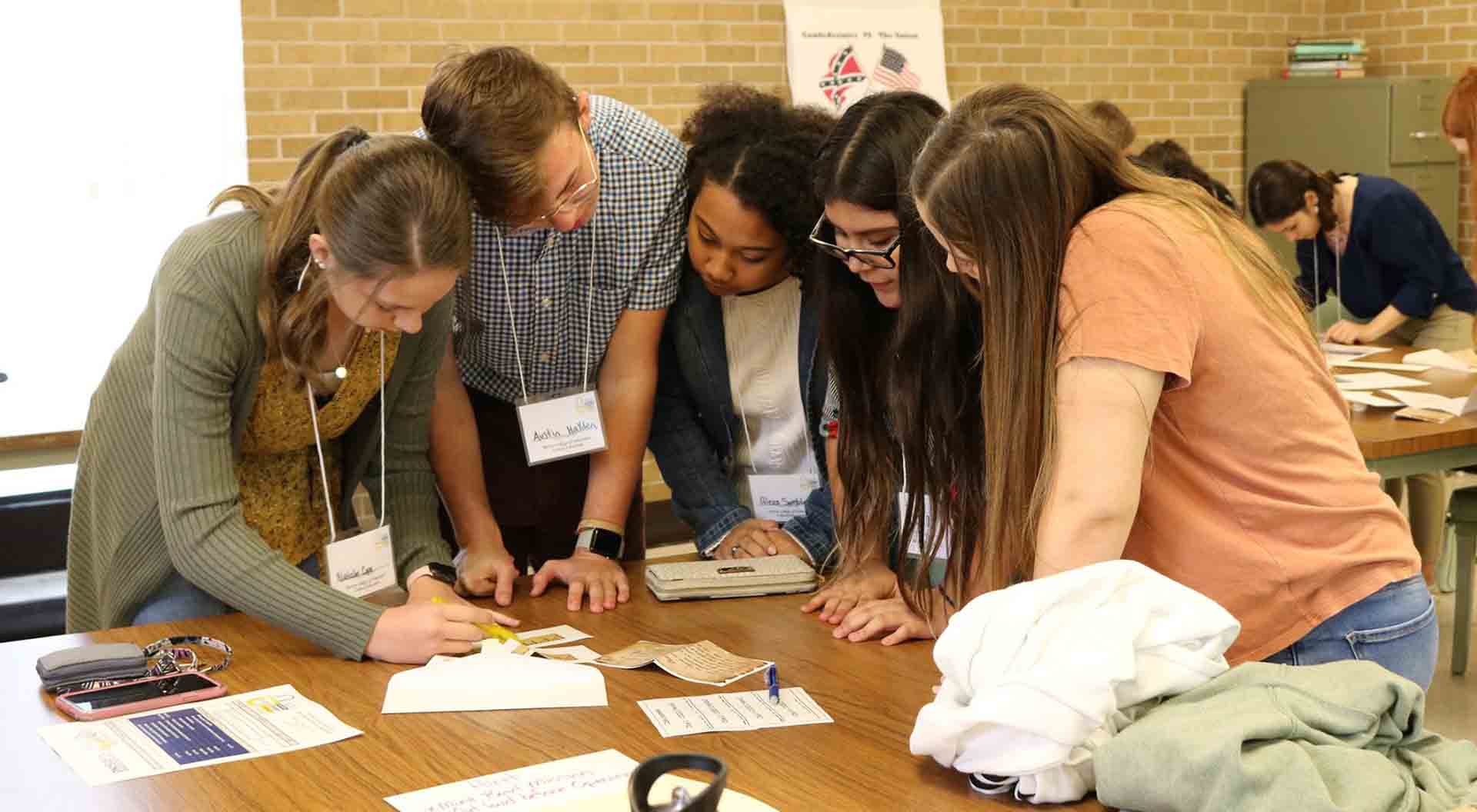 A group of students huddle around to solve a puzzle.