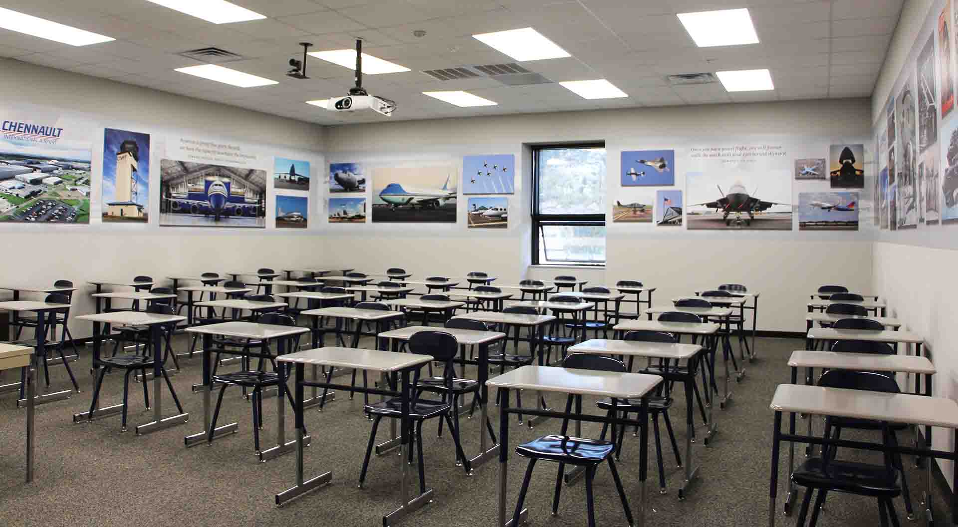 Wide shot of the classroom showing desk and a mural of airplanes