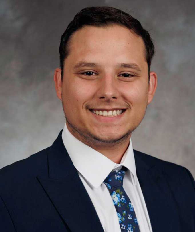 Smiling man in a suit and floral tie, neutral background
