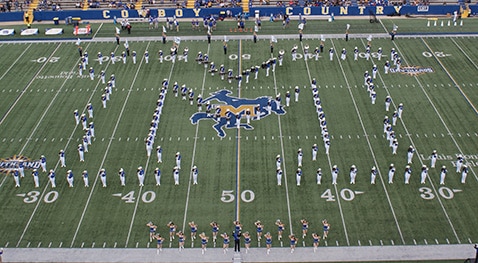 Marching band performing on football field forming patterns, viewed from above in stadium setting.