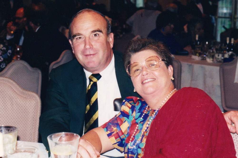 Smiling couple seated at a formal event with tables and guests in the background.