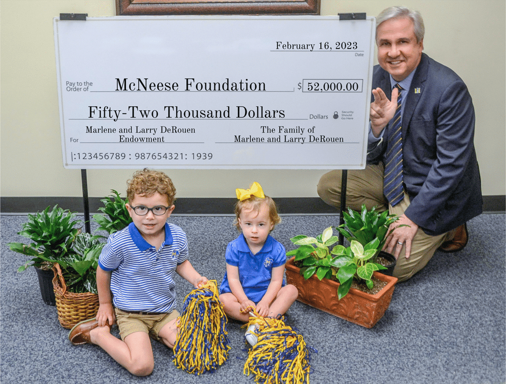 Man with children holding pom-poms near large check for $52,000 donation to McNeese Foundation, surrounded by plants.