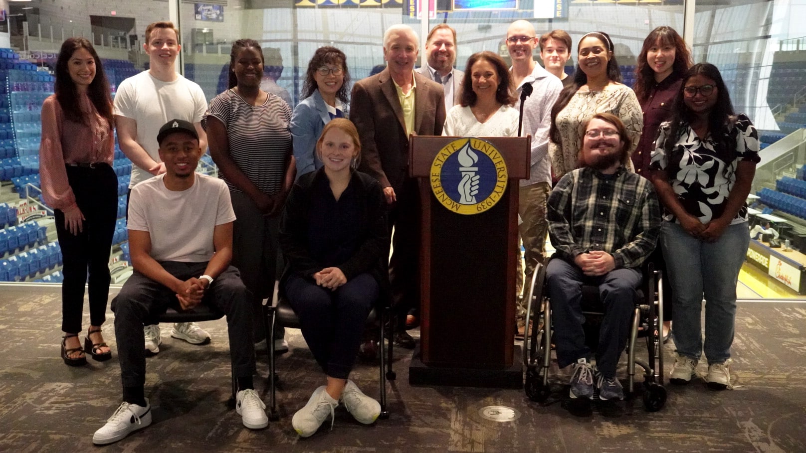Diverse group of students and faculty at McNeese State University standing behind a podium inside a sports arena.