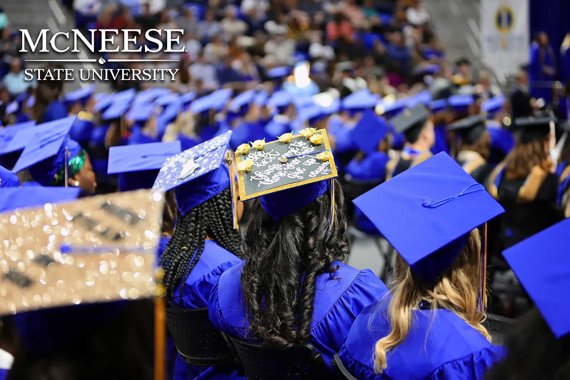 Graduates in blue gowns and custom caps at McNeese State University commencement ceremony.