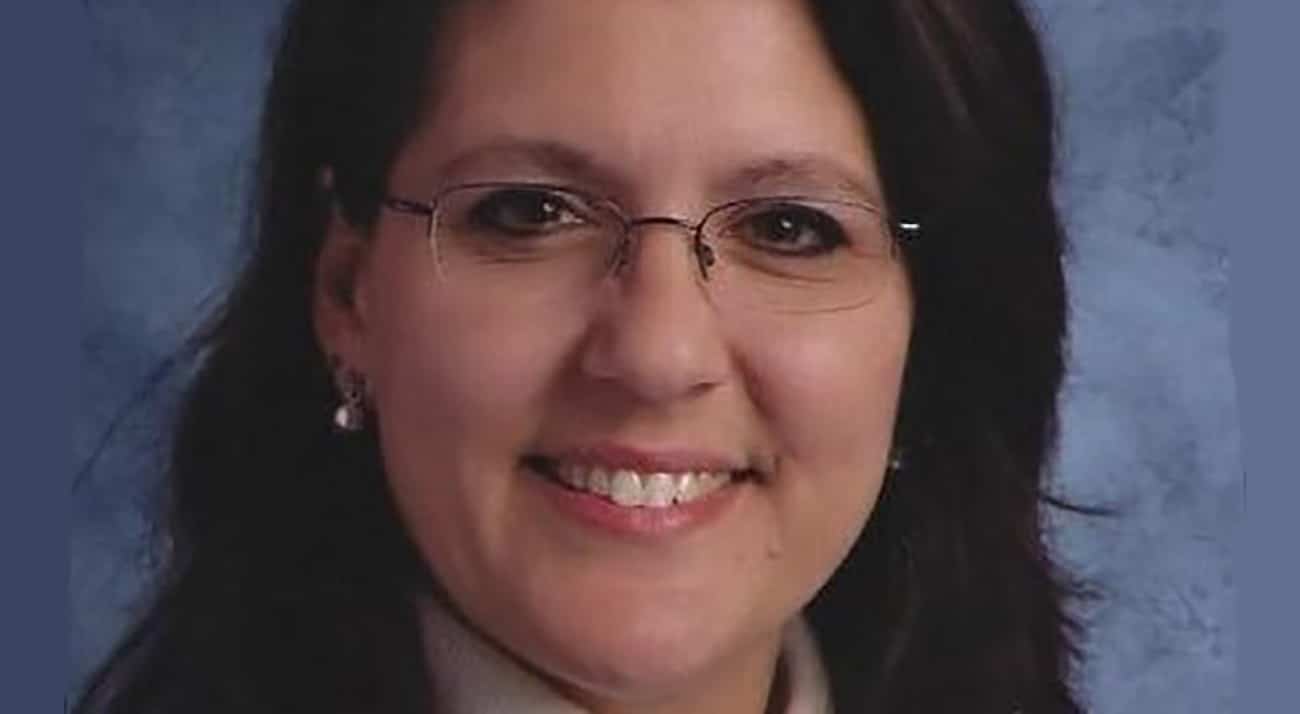 Smiling woman with glasses and dark hair against blue background