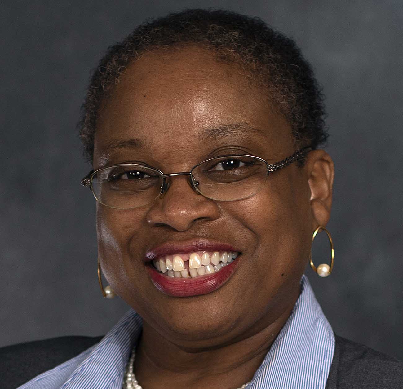 Smiling woman with glasses and pearl earrings against dark background