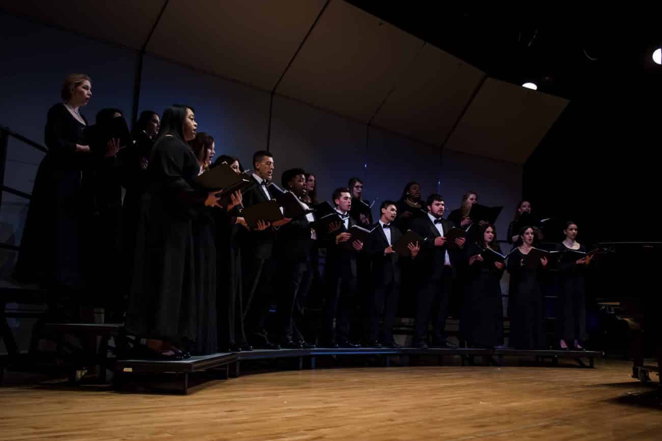 Mixed choir in formal attire performing on stage at a concert.