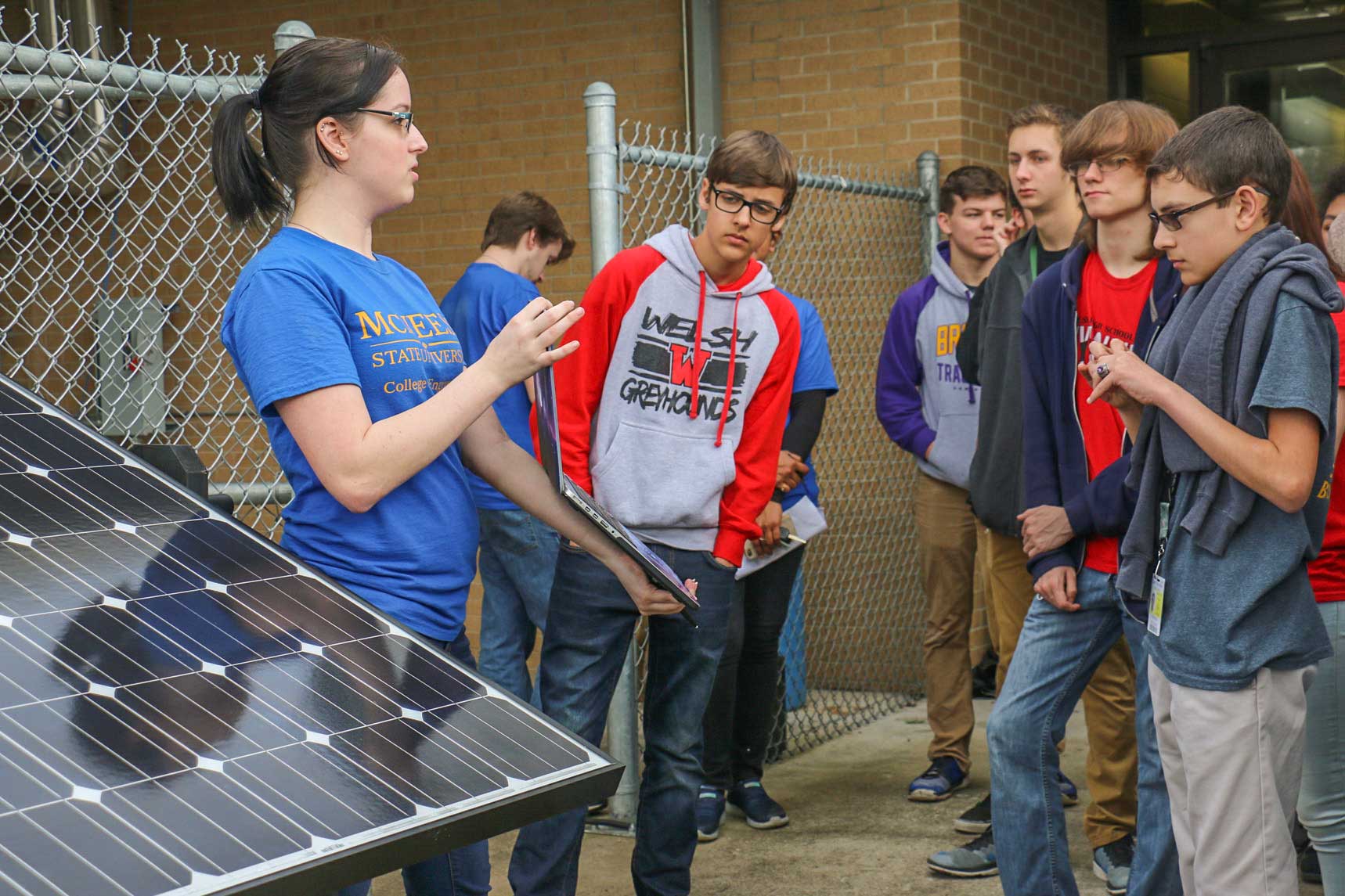 Instructor explains solar panel technology to attentive students outside a school building.