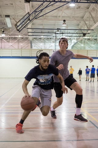 Two men playing intense basketball game indoors, one dribbling while being closely defended.