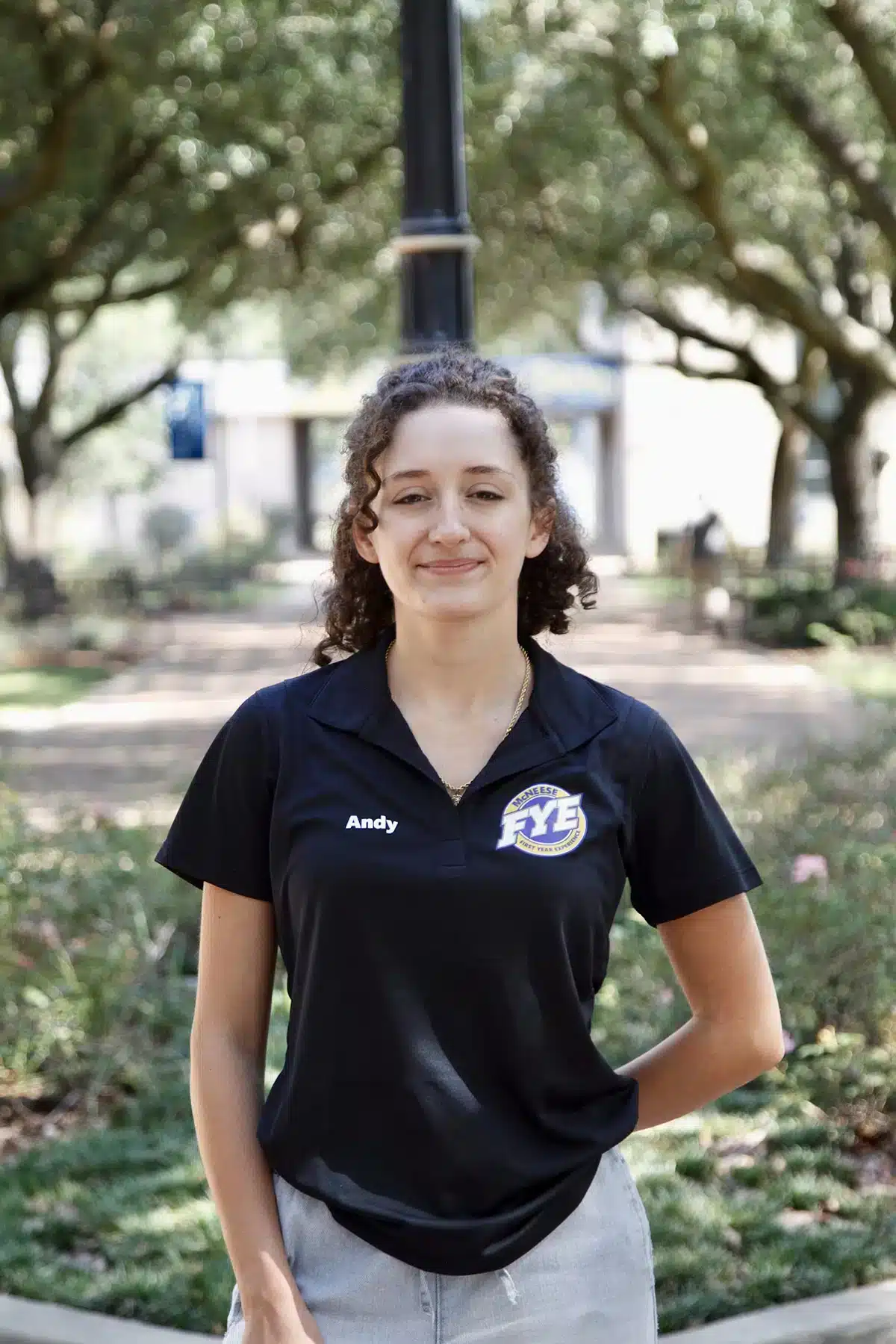 Person with curly hair wearing a black FYE shirt in a park setting.