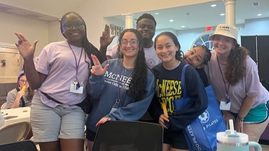 Group of diverse students smiling at McNeese State University event, wearing casual attire indoors.