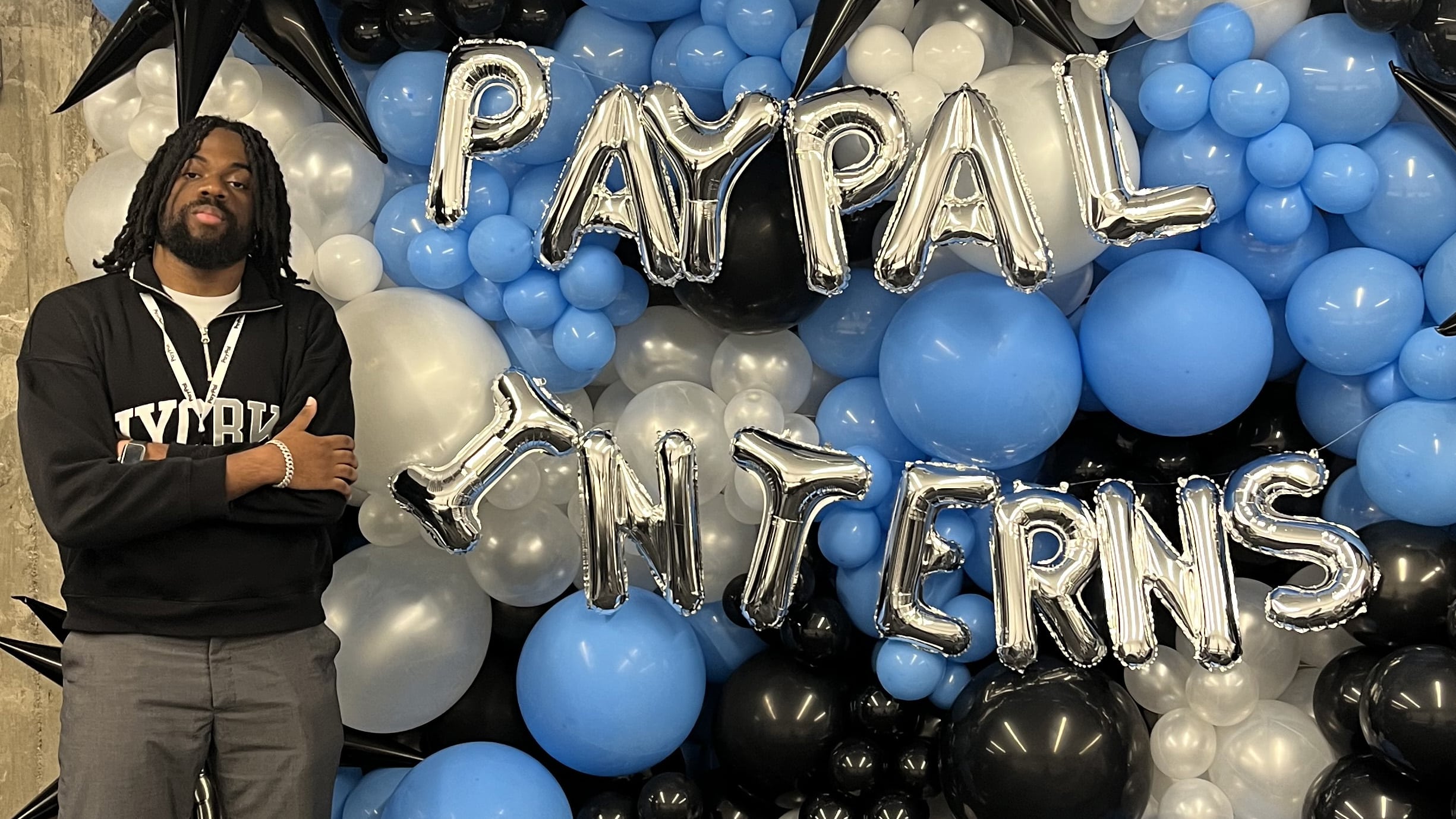 Person standing in front of PayPal Interns balloon display with arms crossed.