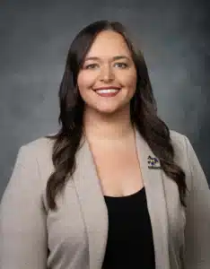 Smiling woman in beige blazer with McNeese State University pin, studio background.