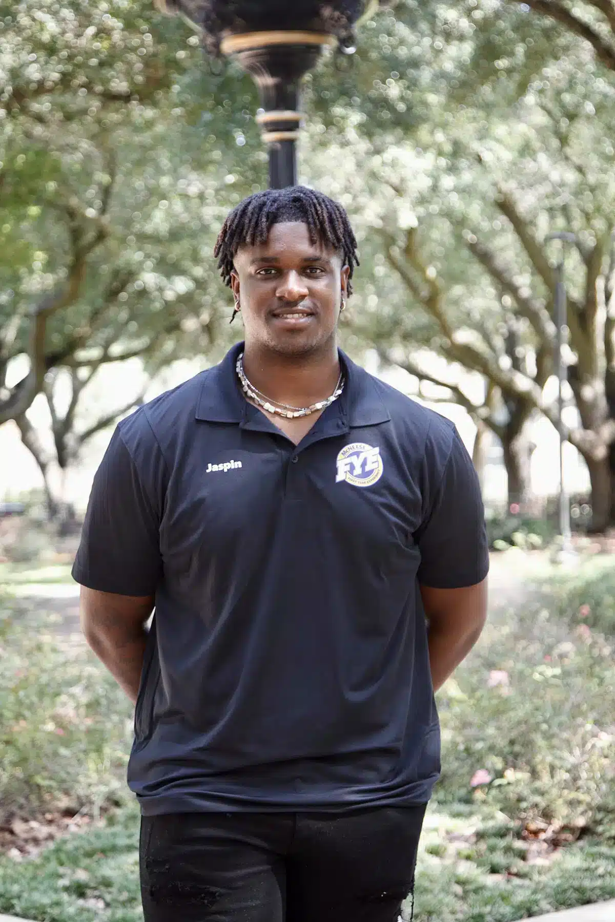 Person in FYL polo shirt stands outdoors with trees in the background.