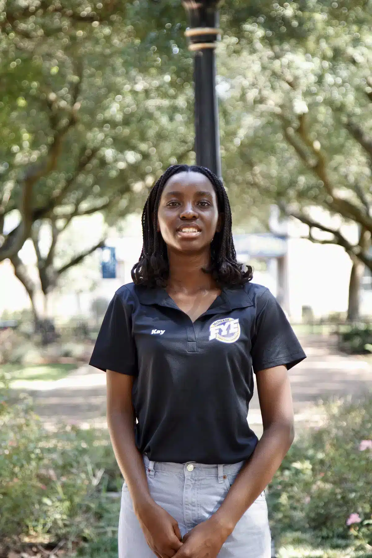 Smiling woman in black polo shirt outdoors with trees in background.