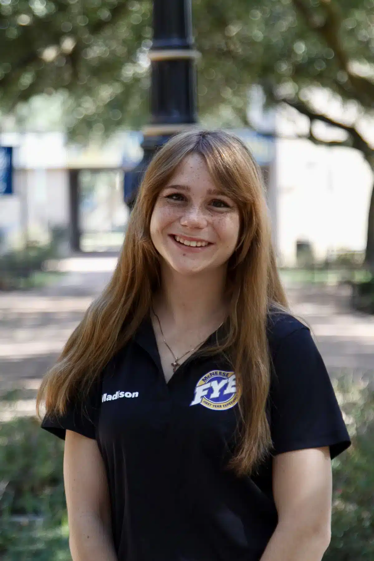 Smiling woman in FYE polo shirt outdoors with blurred trees in background