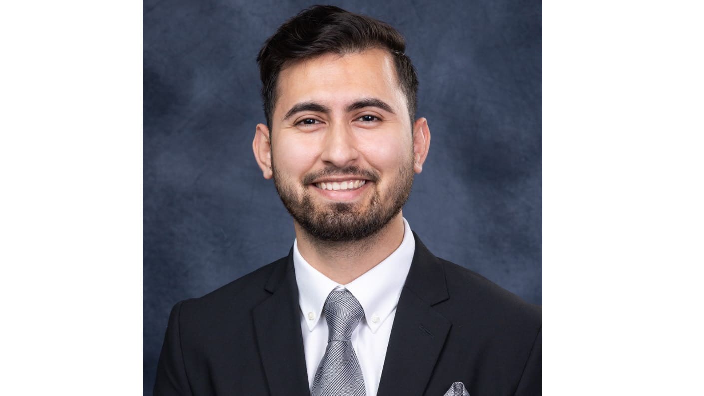 Man in suit and tie smiling against dark background.