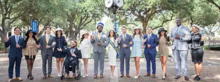 Diverse group of well-dressed individuals smiling and linking arms in a park setting with trees and a decorative clock.