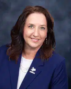 Smiling woman in a blue blazer with dark hair against a dark background