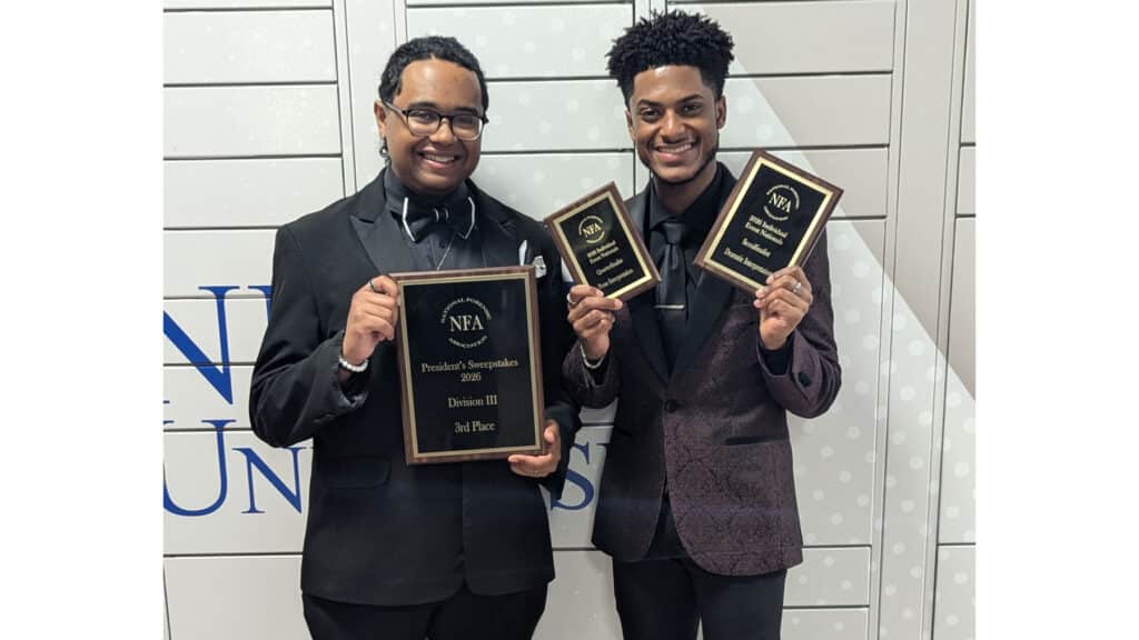 McNeese students dressed in black suits hold up plaques they won in a speech and debate tournament.