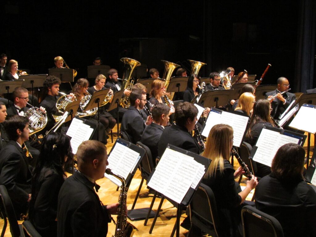Orchestra performing on stage with musicians playing various brass and woodwind instruments.