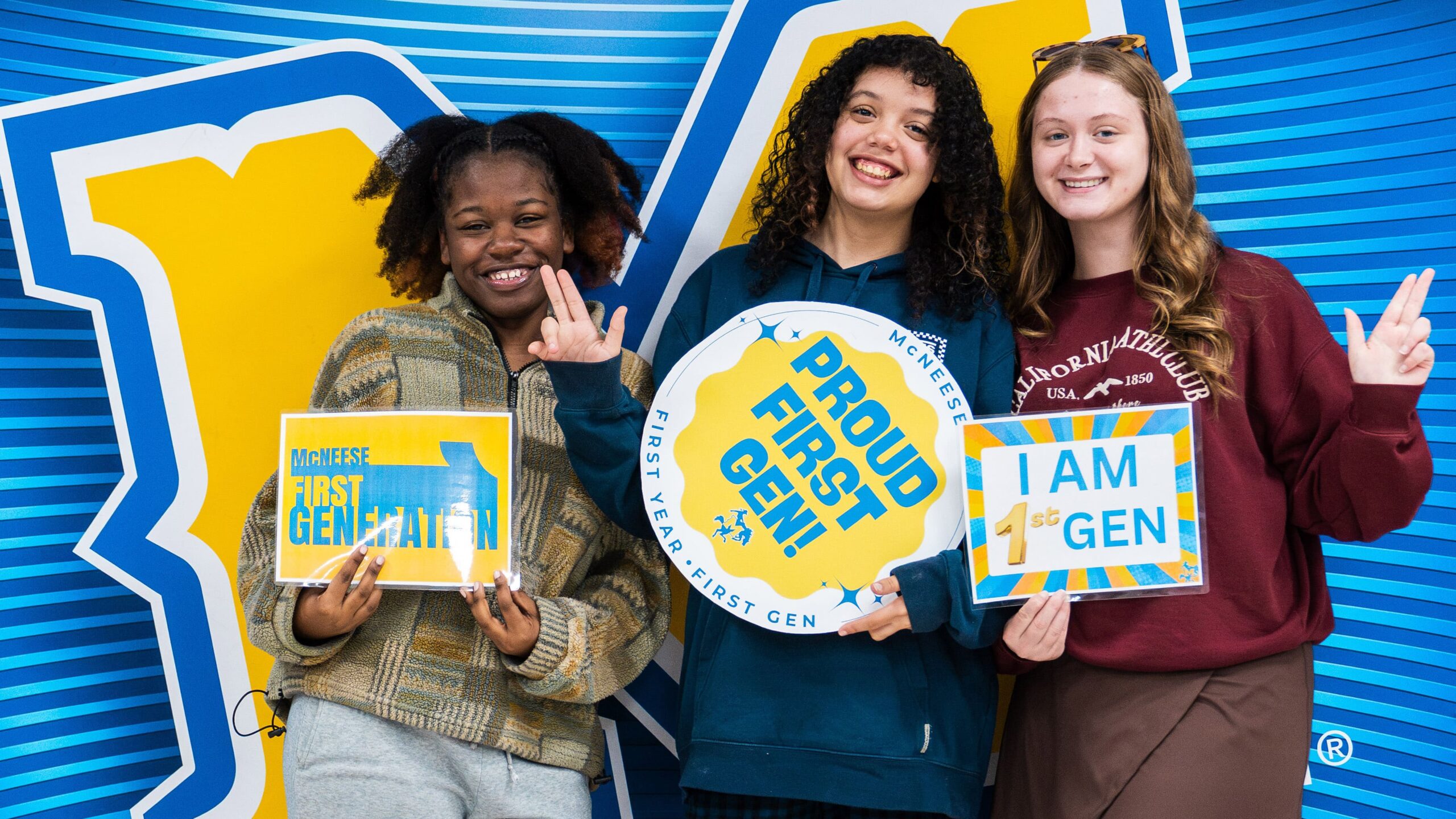 Three students smiling, holding signs celebrating being first-generation college students at an event.
