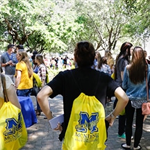 Group of students with McNeese backpacks in an outdoor campus event with trees and people interacting.