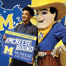Smiling student poses with McNeese State University mascot, holding #McNeeseBound sign at campus event.