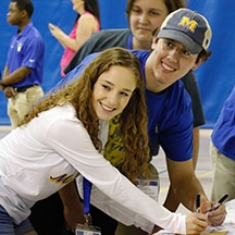 Young people smiling and signing papers at an event, wearing casual attire with name badges.