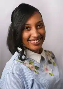 Smiling person with embroidered floral shirt against neutral background