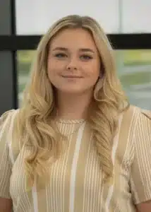 Smiling woman with long blonde hair in a striped shirt, indoors.