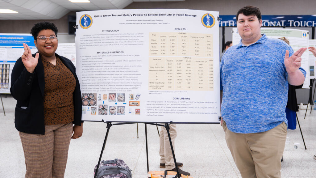 A female and a male student stand with their poster that explains their research.