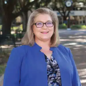 Smiling woman in blue blazer outdoors with blurred background.